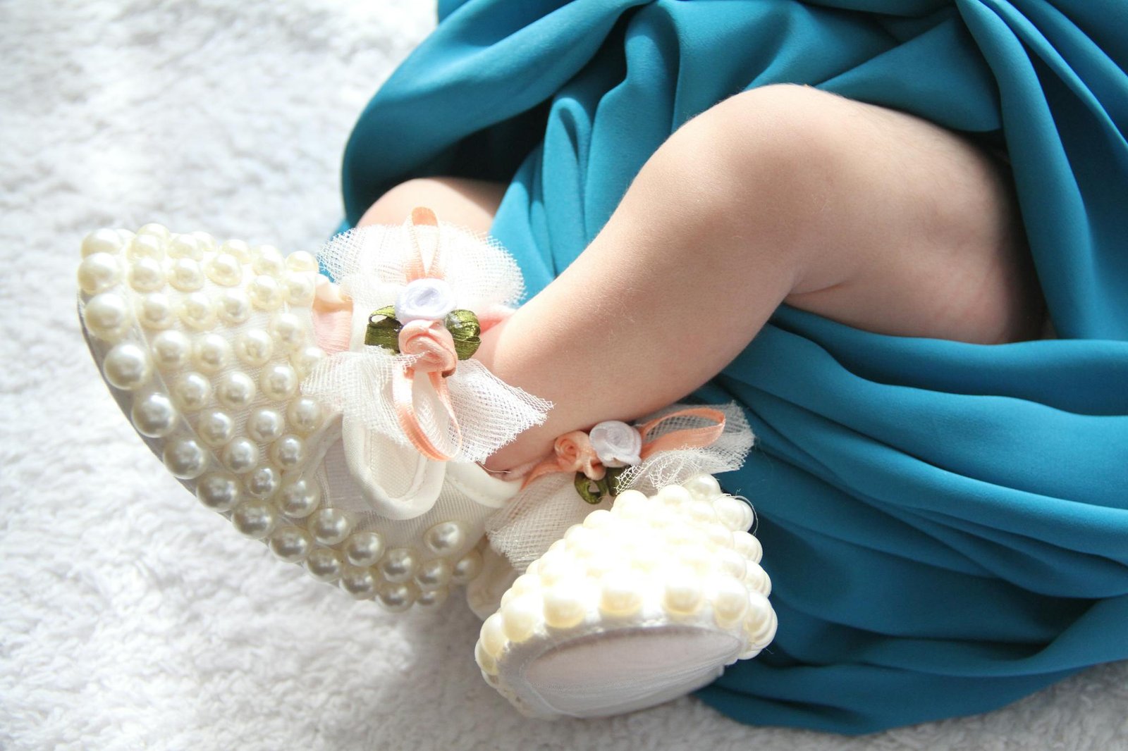 Charming baby feet adorned with pearl-decorated shoes wrapped in a vibrant blue blanket.