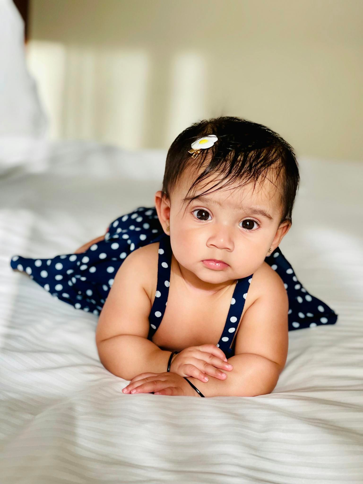 Cute baby in polka dot dress lying on a bed, capturing a sweet moment indoors in Abu Dhabi.