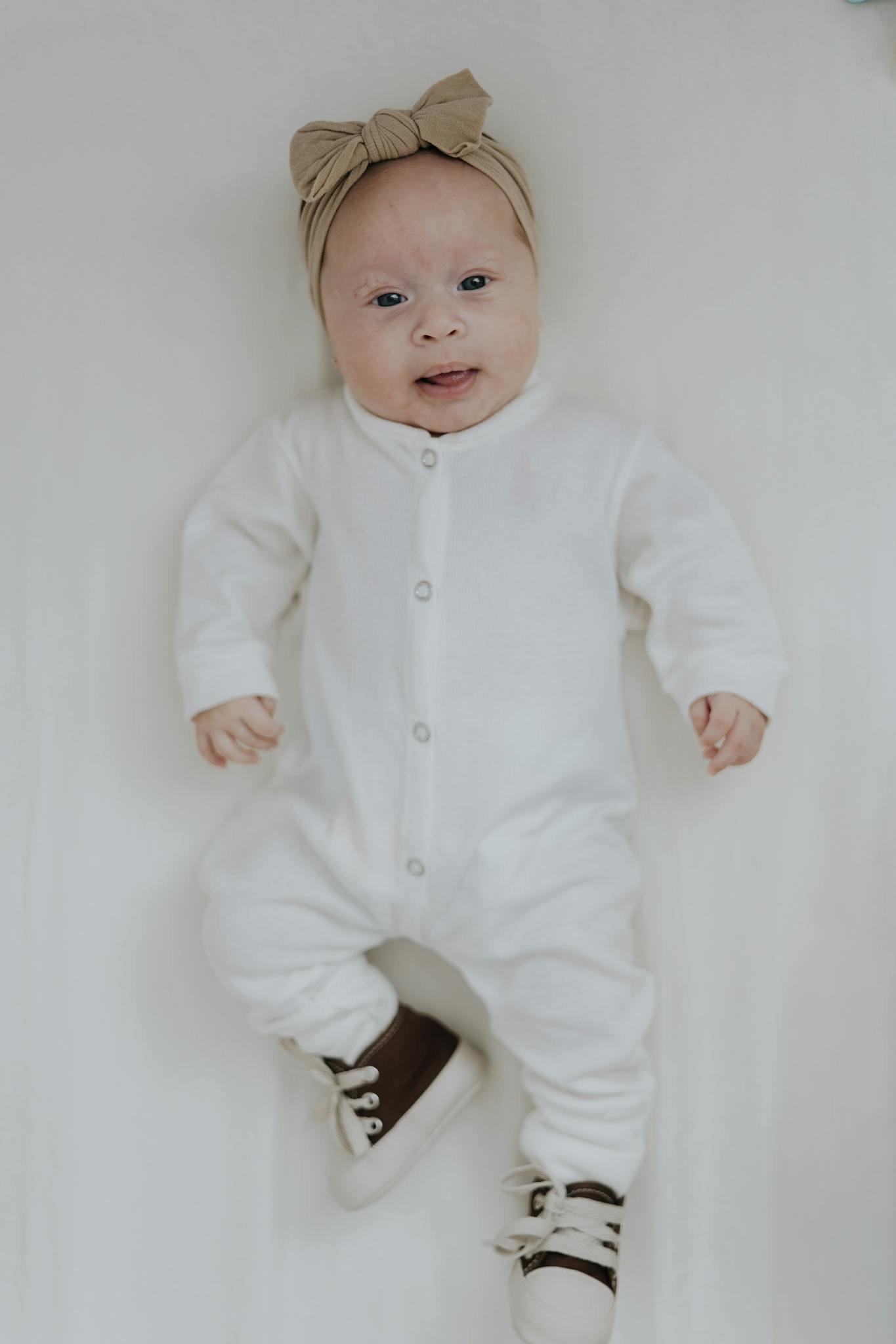 Cute baby lying on a white background wearing a bodysuit and headband.