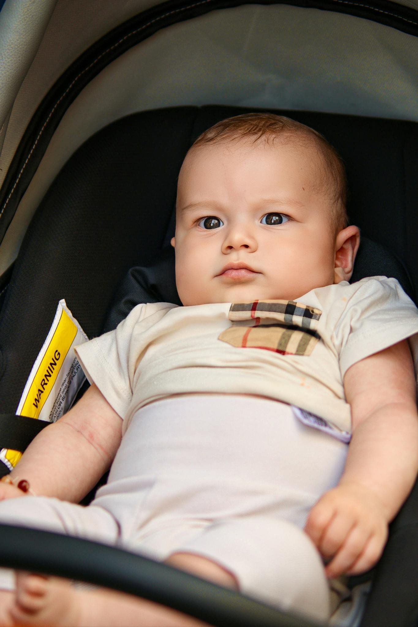 Cute baby relaxing in a stroller wearing a stylish checkered outfit, looking curious and content.