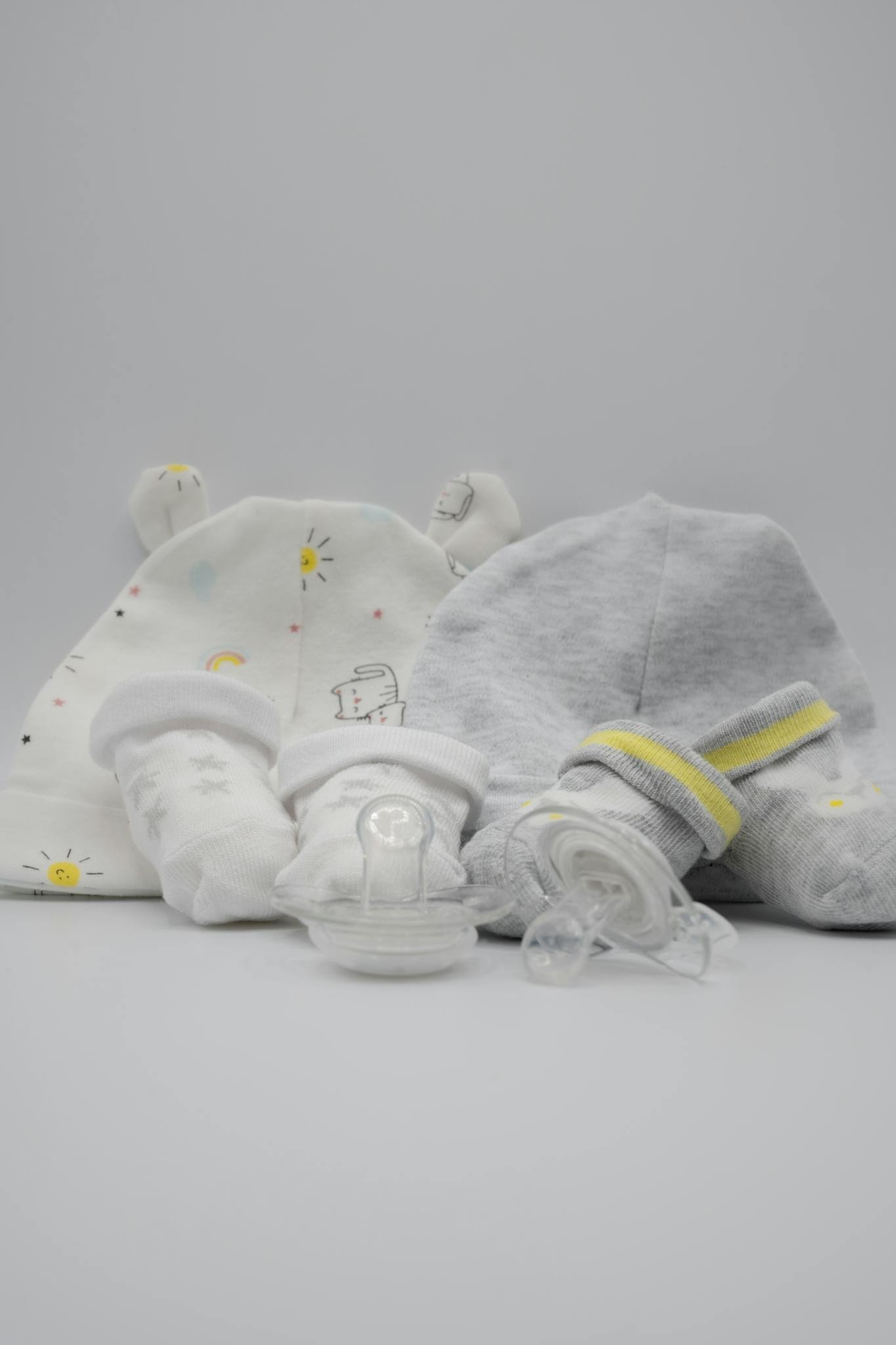 Soft baby socks, bonnets, and pacifiers arranged on a white surface.